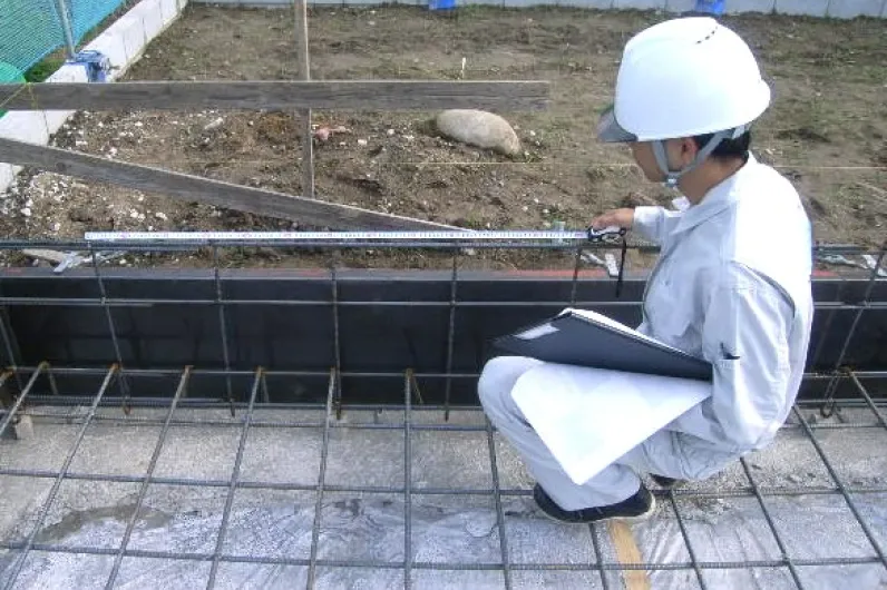 基礎配筋検査の作業風景（メジャーで寸法を測定する検査員）